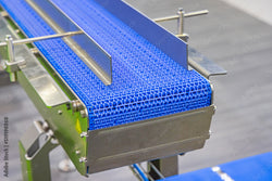 A close-up of a metal industrial conveyor system with a segment of blue plastic modular belting on it.